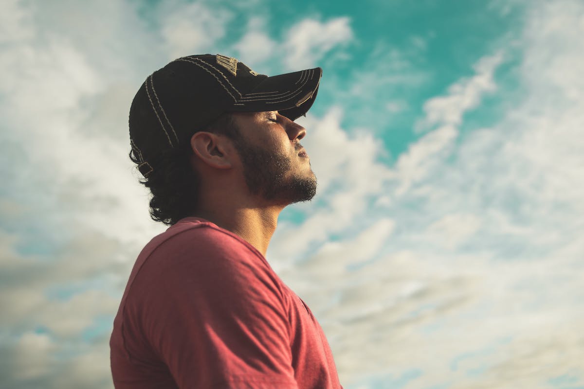 a man in a baseball cap taking a deep breath looking at the sky